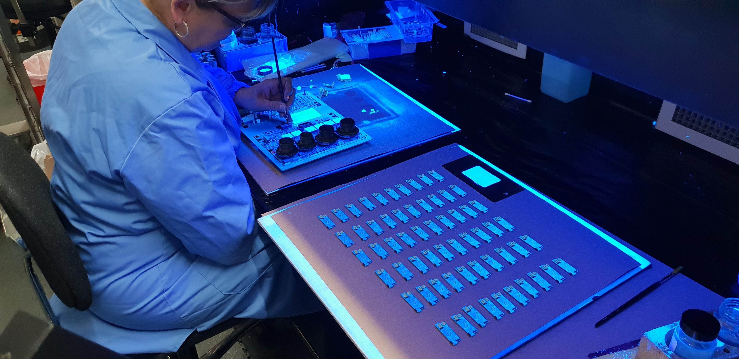 A PCB being inspected inside a IB101 UV Inspection Booth under UVA light